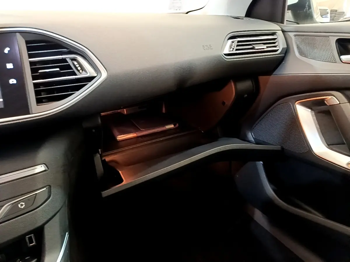 Intérieur de la Peugeot 308 blanc, vue côté passager avec boîte à gants ouverte et tableau de bord noir.