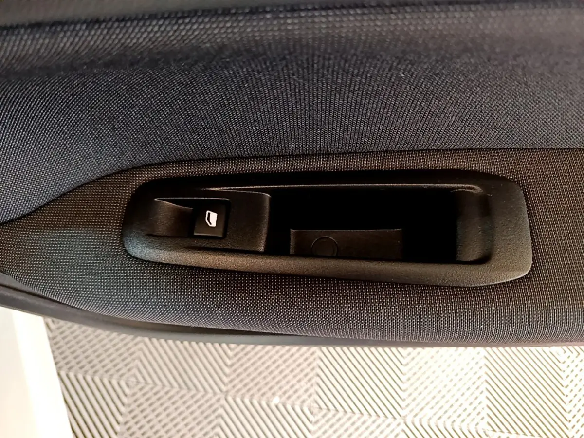 Poignée intérieure de coffre noir sur tissu gris foncé dans une Peugeot 308 blanche, vue en gros plan.