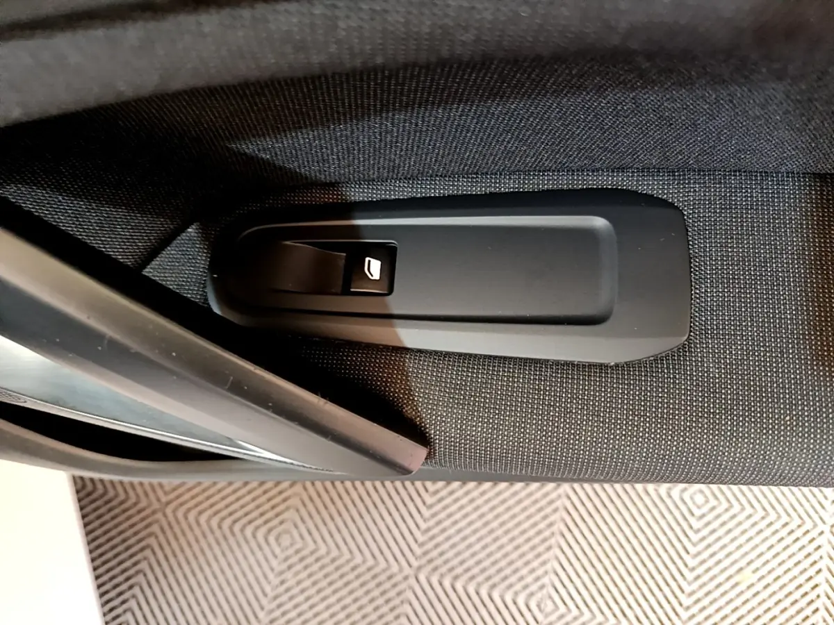 Gros plan sur la poignée de déverrouillage de porte intérieure noire sur tissu gris d'une Peugeot 308 blanche.