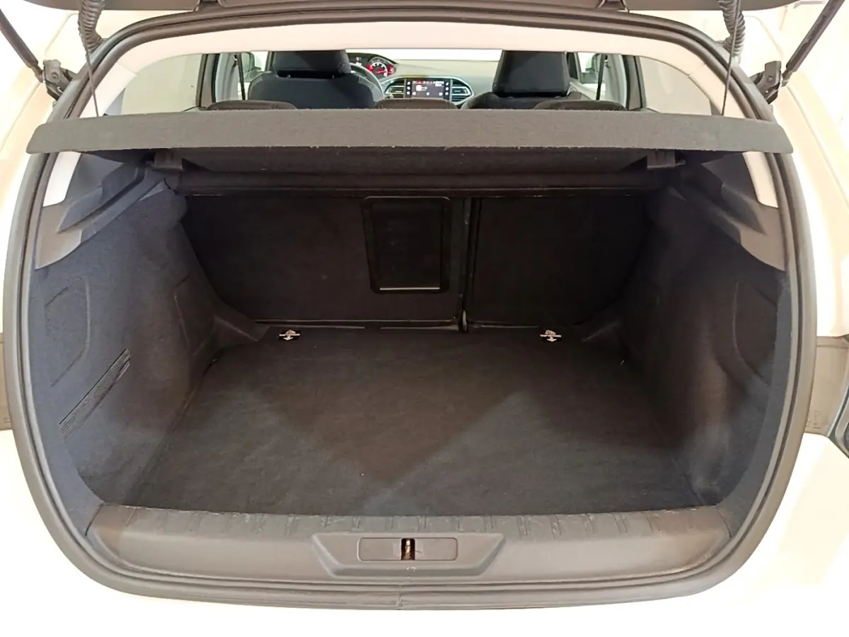 Coffre ouvert d’une Peugeot 308 blanche, vue arrière montrant l’espace de chargement et la trappe à ski au fond.