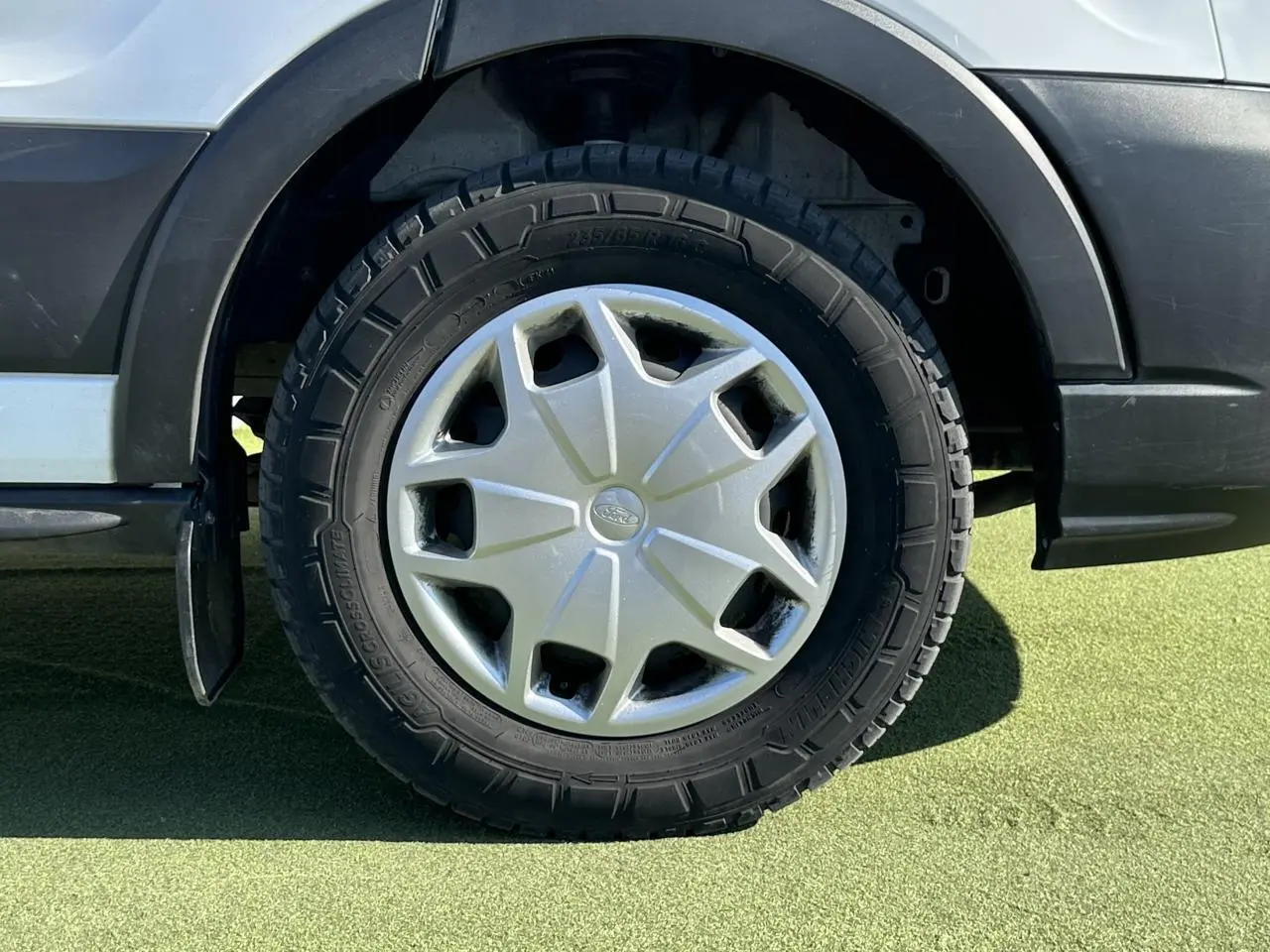 Gros plan sur la roue arrière gauche du Ford Transit Fourgon blanc, avec enjoliveur argenté et pneu tout-terrain.