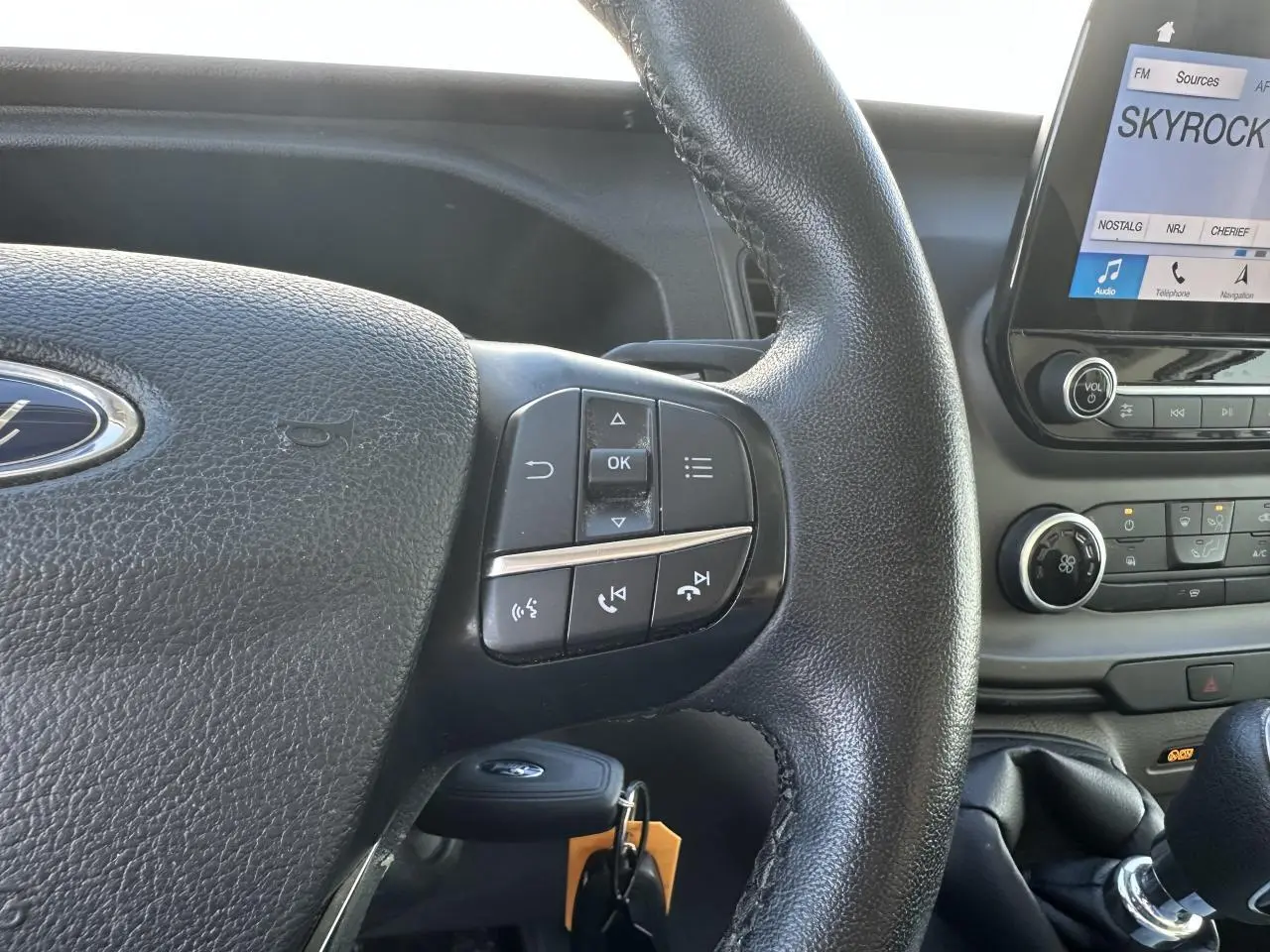 Gros plan sur le volant noir et la console centrale du Ford Transit Fourgon blanc, avec écran tactile affichant Skyrock.