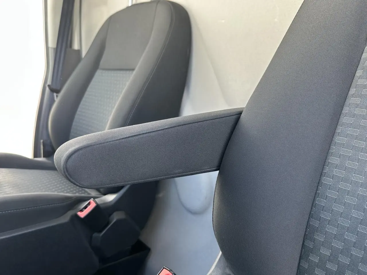 Gros plan sur les sièges avant gris foncé du Ford Transit Fourgon blanc, avec accoudoir relevable côté droit.