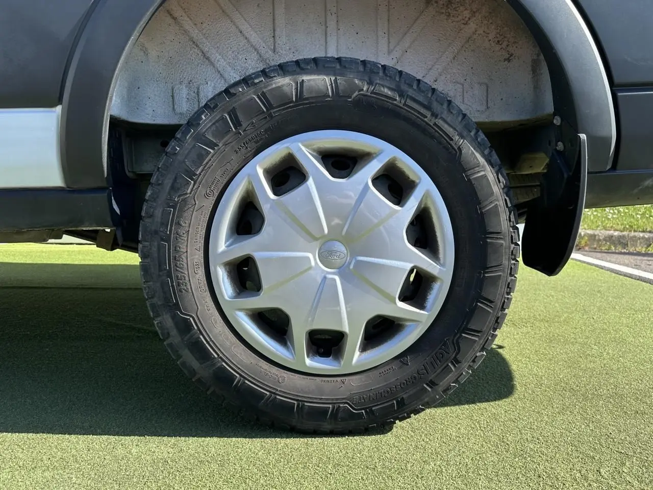 Gros plan sur la roue arrière droite du Ford Transit Fourgon blanc, avec enjoliveur argenté et pneu tout-terrain.
