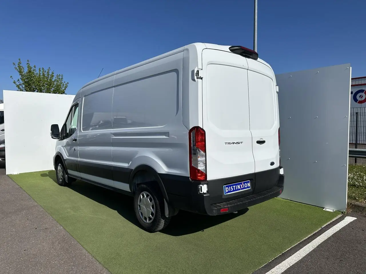 Fourgon Ford Transit blanc en vue 3/4 arrière droit, avec pare-chocs noir et porte latérale coulissante visible.