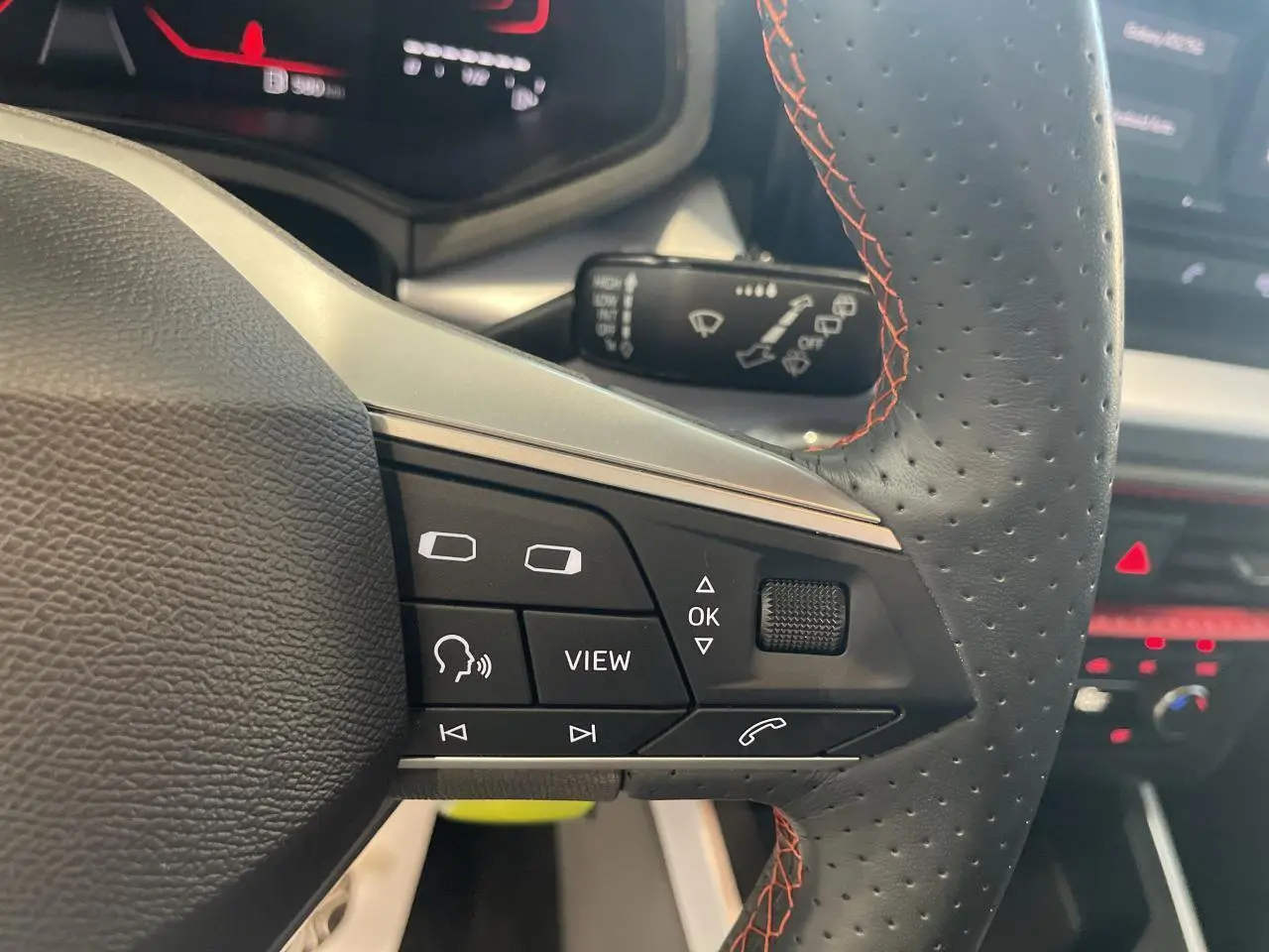 Gros plan sur le volant sport cuir noir perforé avec surpiqûres rouges du SEAT Arona 2024, boutons multifonctions visibles.