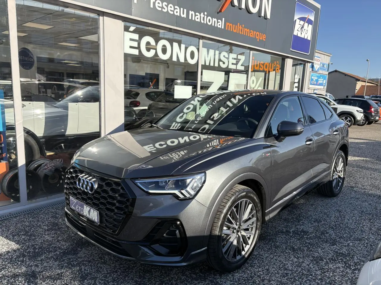 Audi Q3 Sportback gris Daytona en 3/4 avant droit avec calandre noire et jantes 20 branches contrastées.