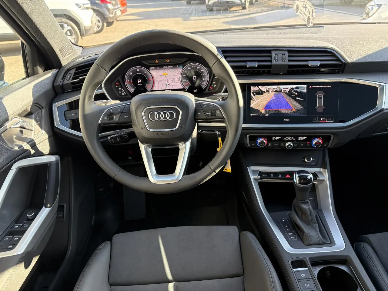 Vue intérieure avant de l'Audi Q3 Sportback 2025, volant cuir, tableau de bord numérique et écran central affichant la caméra de recul.
