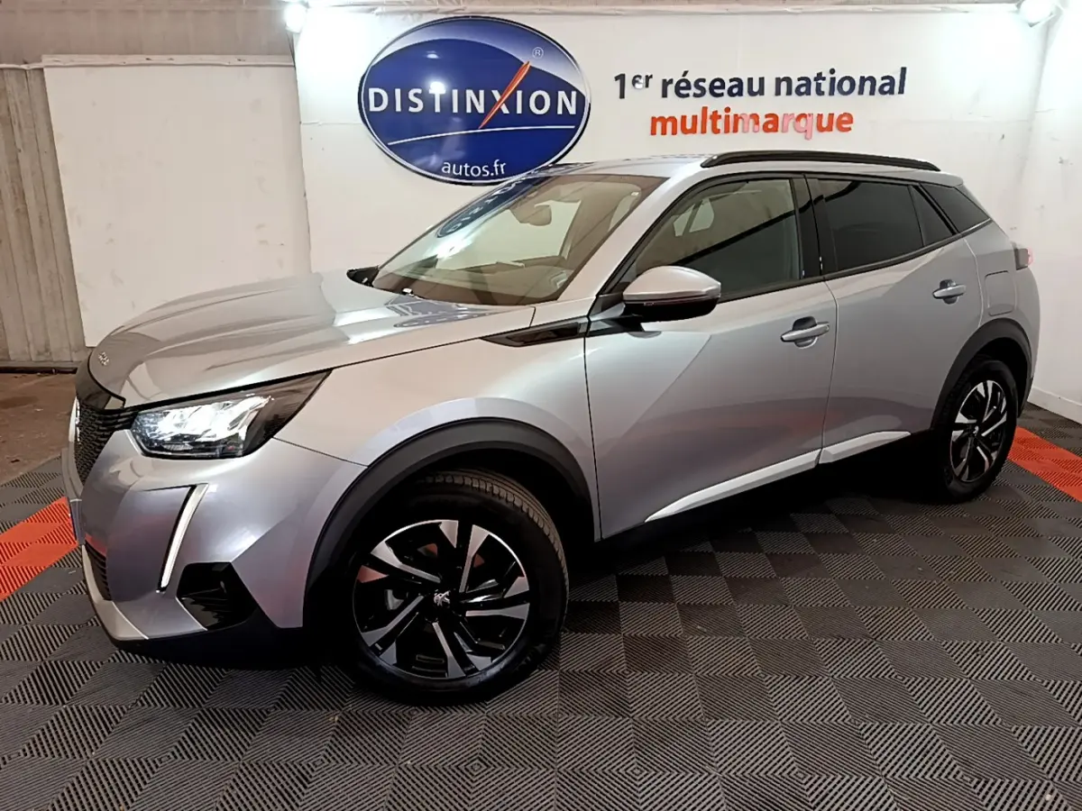 Peugeot 2008 gris clair en 3/4 avant droit, avec jantes noires et toit noir, dans un showroom intérieur.