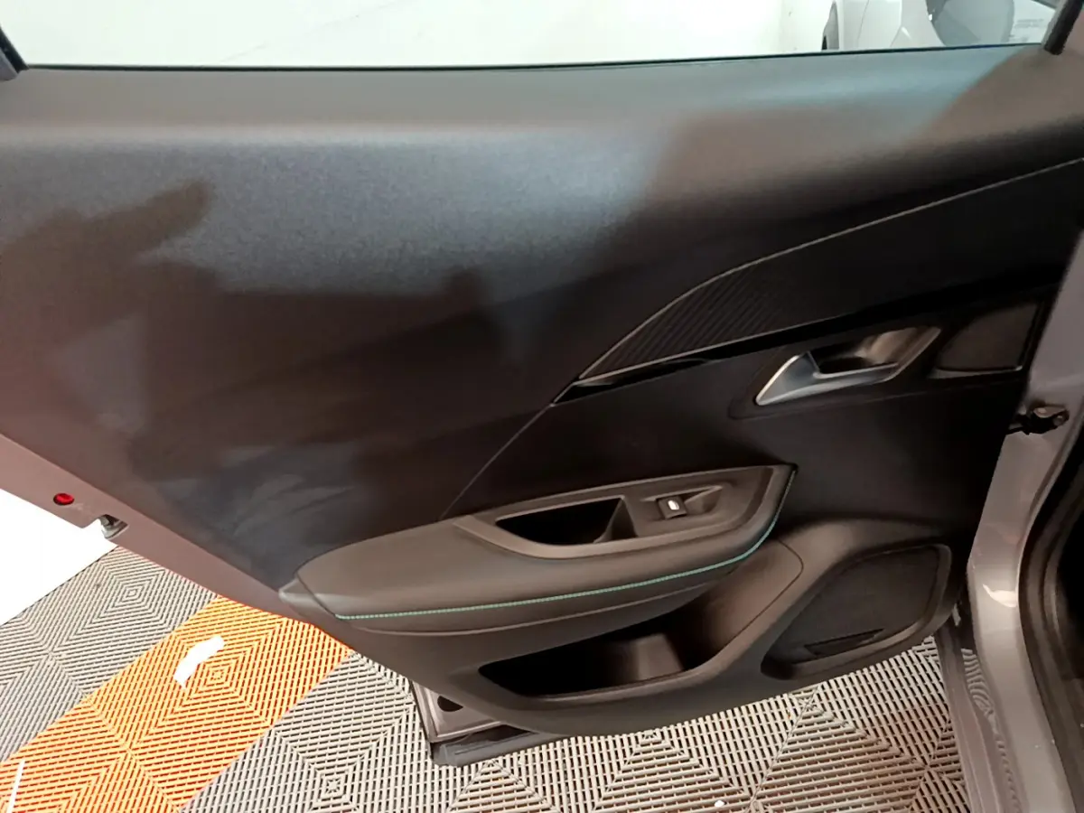 Vue intérieure de la porte côté gauche du Peugeot 2008 gris clair, avec garniture noire et surpiqûres bleues.