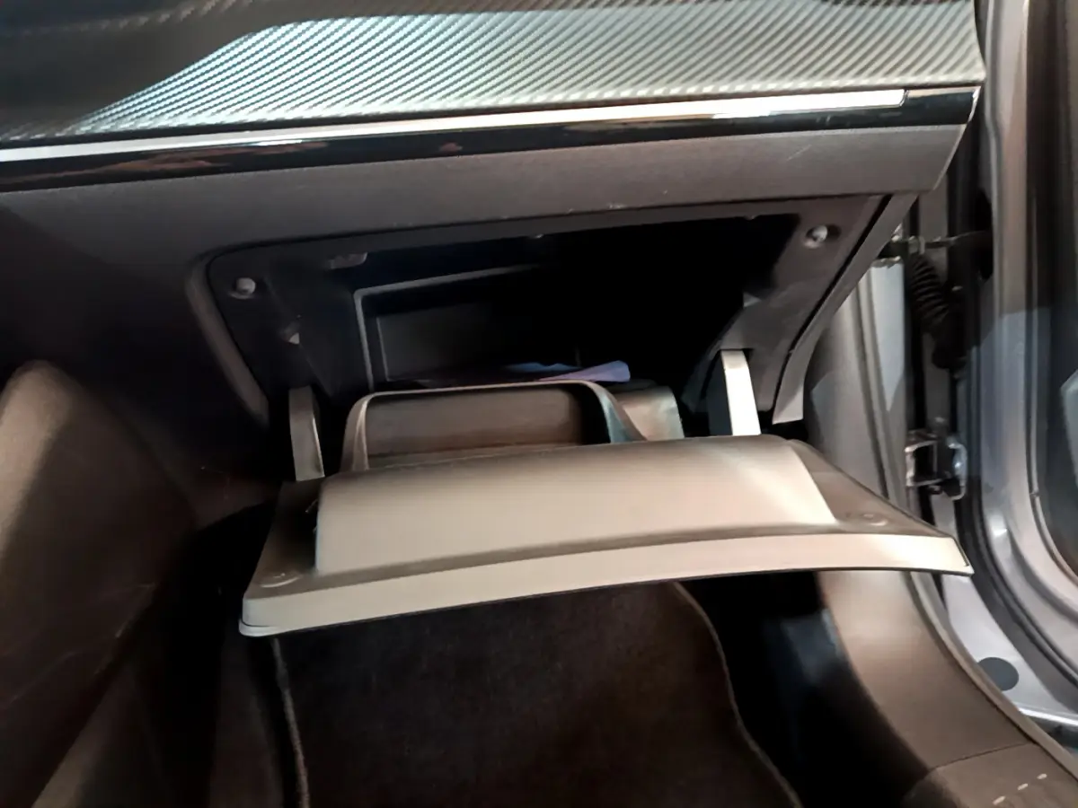 Gros plan sur la boîte à gants ouverte côté passager du Peugeot 2008 gris clair, soulignant l'intérieur noir.
