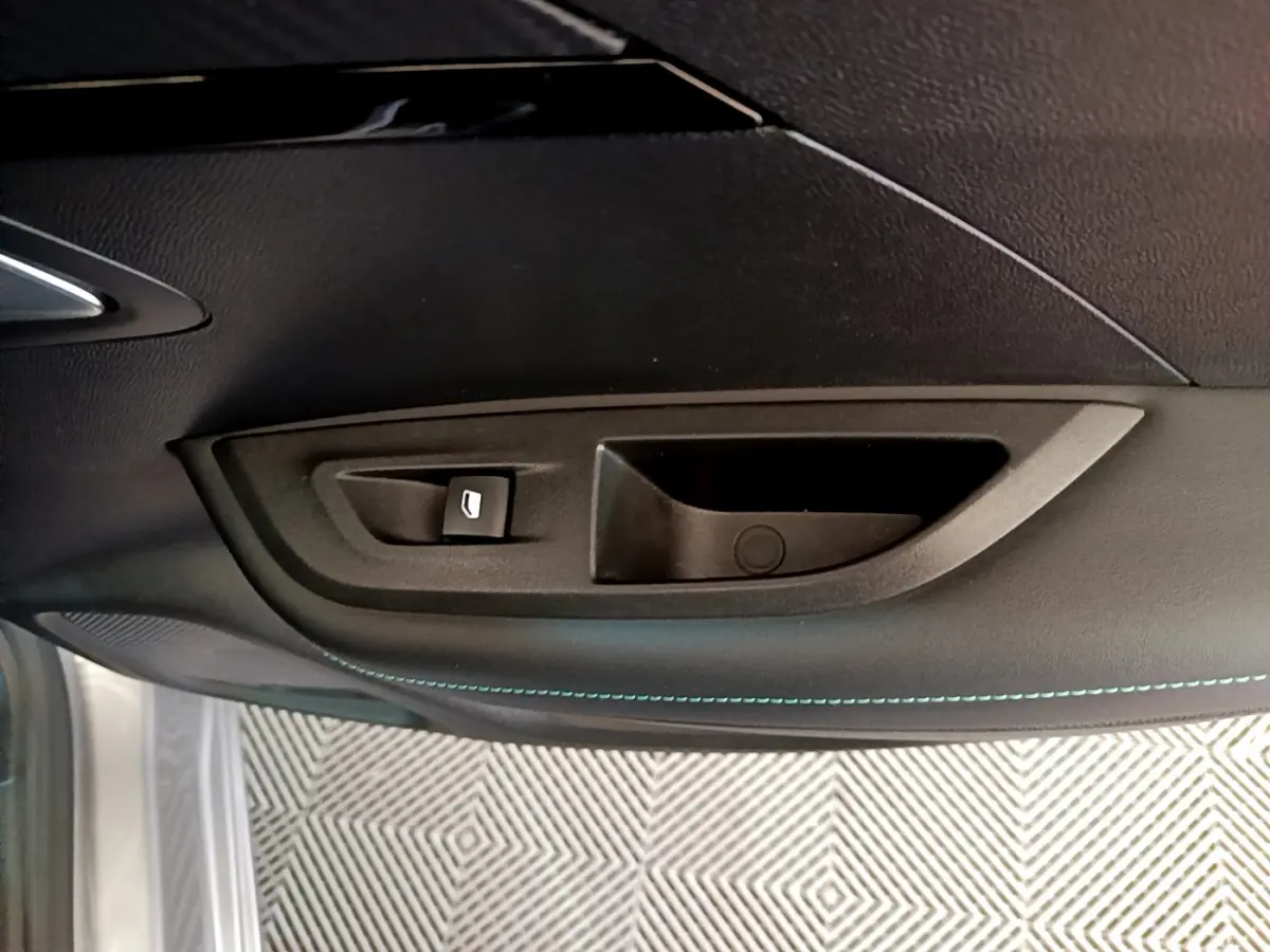 Poignée intérieure de porte côté gauche du Peugeot 2008 gris clair, avec bouton de commande de vitre et surpiqûres bleues.