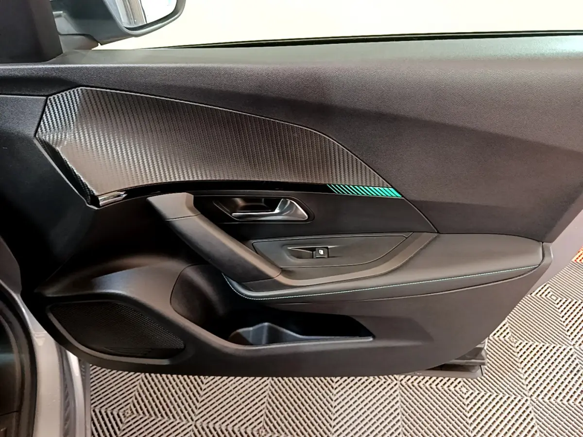 Intérieur côté gauche de porte Peugeot 2008 gris clair, avec insert décor carbone et bouton de lève-vitre.