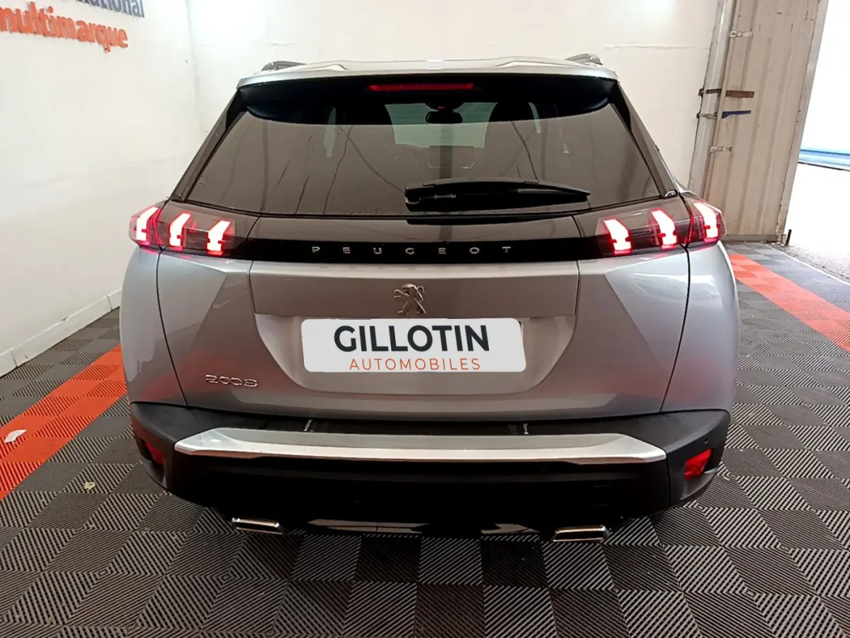Vue arrière d'un Peugeot 2008 gris clair 2021 avec feux LED allumés dans un garage showroom.