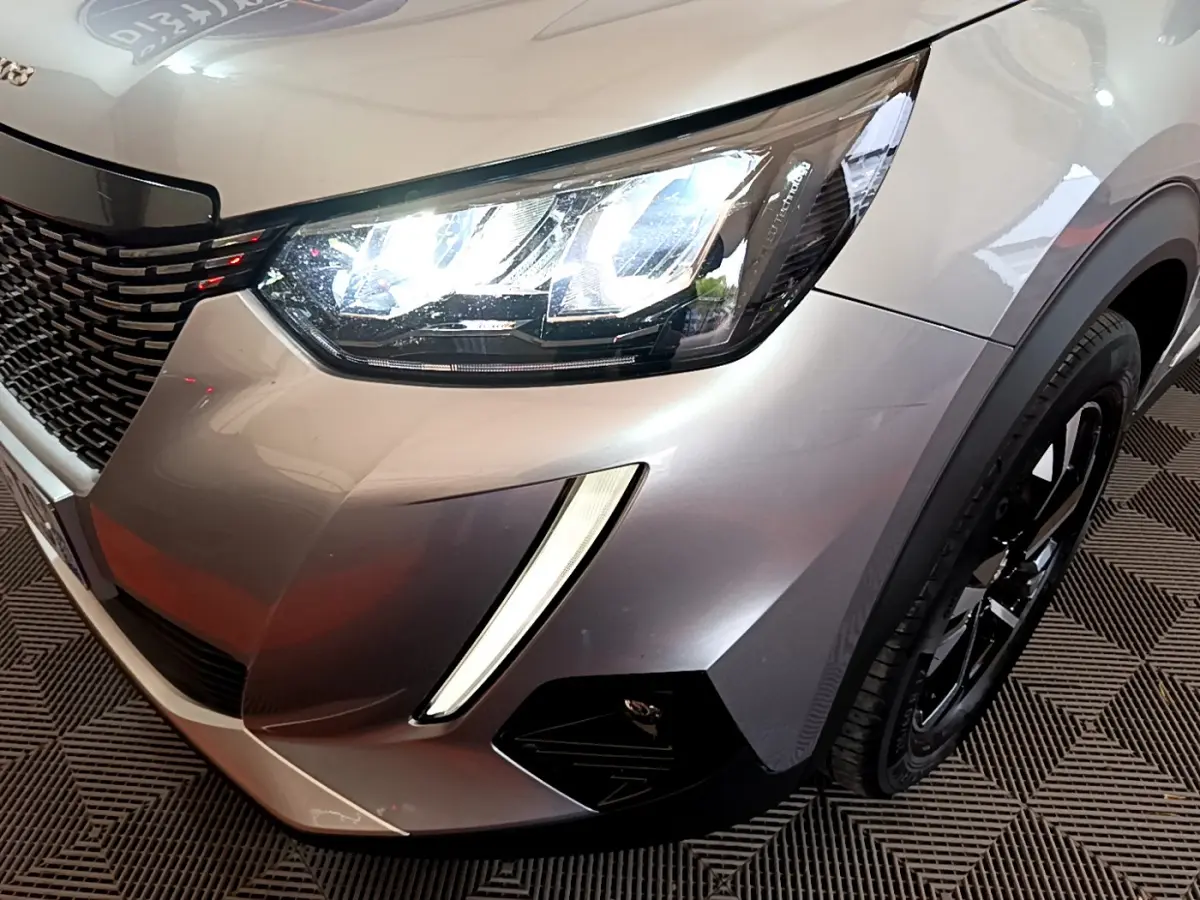 Gros plan sur l'avant droit gris clair du Peugeot 2008 avec ses phares LED allumés et la calandre noire.
