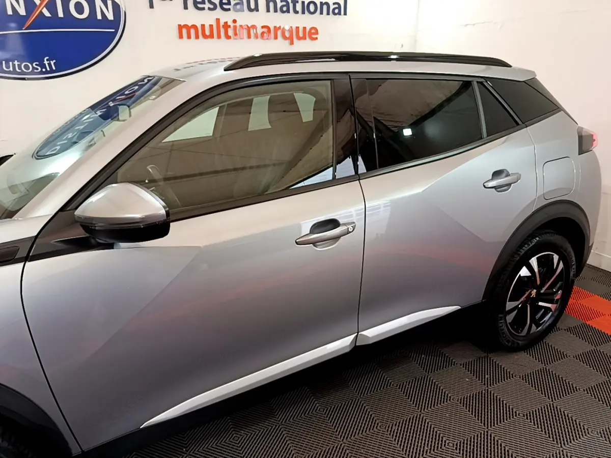 Profil côté gauche du Peugeot 2008 gris clair avec vitres teintées et jantes noires à motifs rouges.