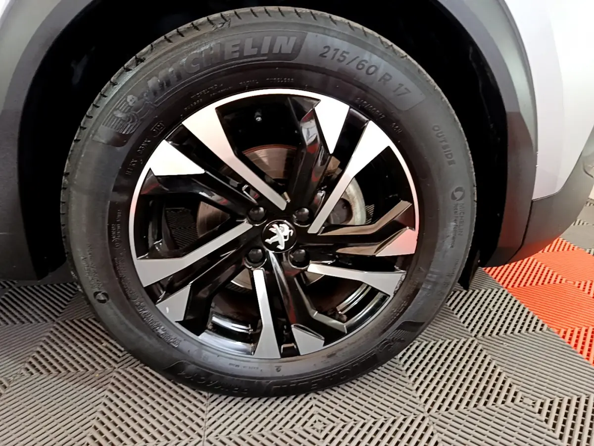 Gros plan sur la roue avant droite du Peugeot 2008 gris clair, mettant en valeur la jante alliage noire et argentée au design moderne.