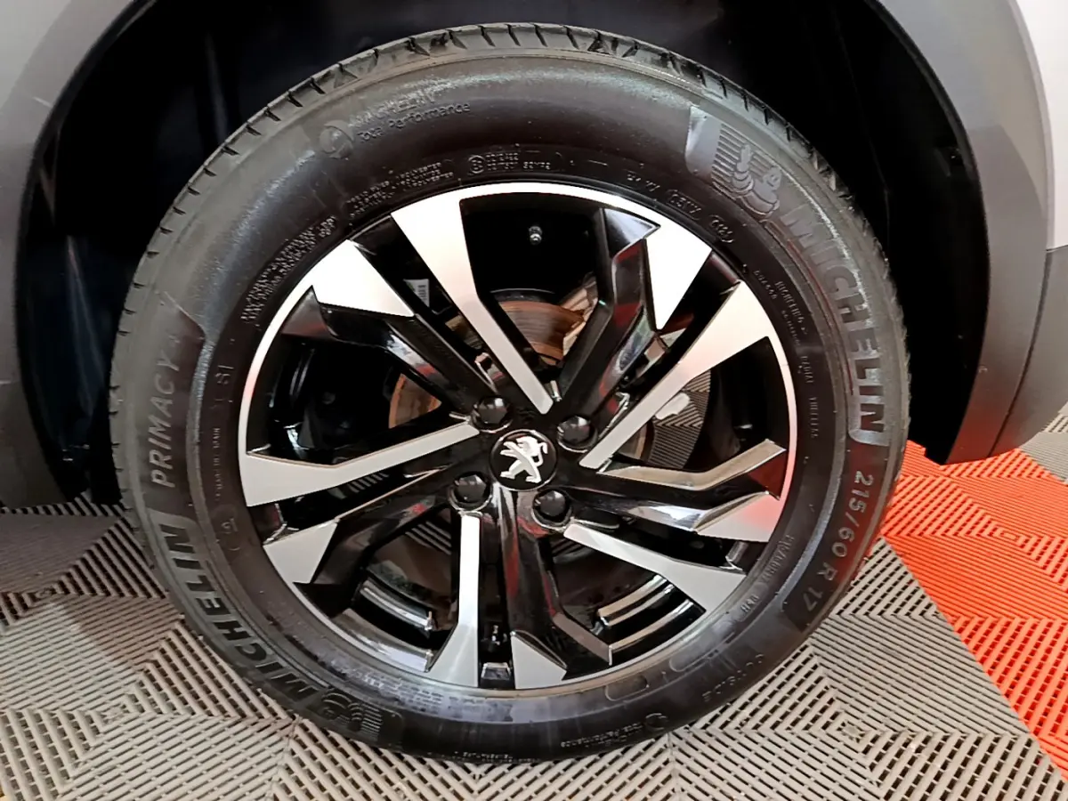 Gros plan sur la jante noire et argentée avec logo Peugeot d'un Peugeot 2008 gris clair, pneu Michelin visible.