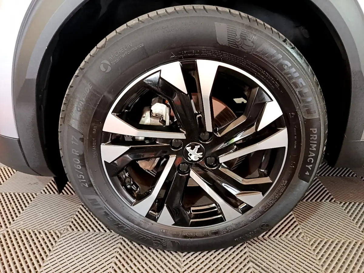 Gros plan sur la roue avant gauche du Peugeot 2008 gris clair, avec jante alliage noire et argentée au design moderne.