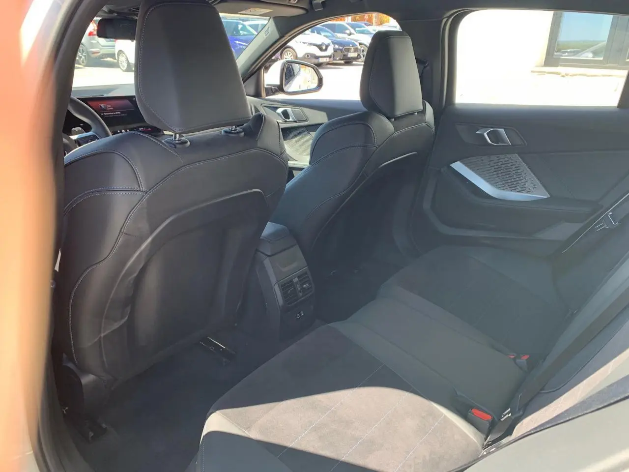 Vue intérieure arrière droite de la BMW Série 1 118D M Sport 2025 avec sellerie Alcantara noire et surpiqûres bleues.