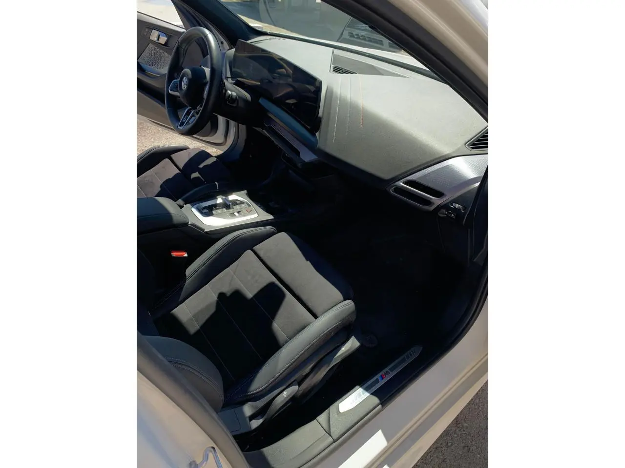 Intérieur côté conducteur de la BMW Série 1 blanche, avec sièges sport Alcantara et tableau de bord moderne M Sport.