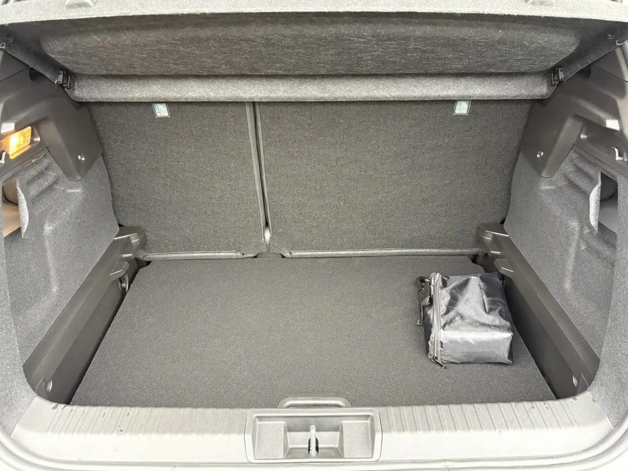 Coffre ouvert vu de face d’un Renault Captur blanc nacré, avec un sac noir posé à droite.