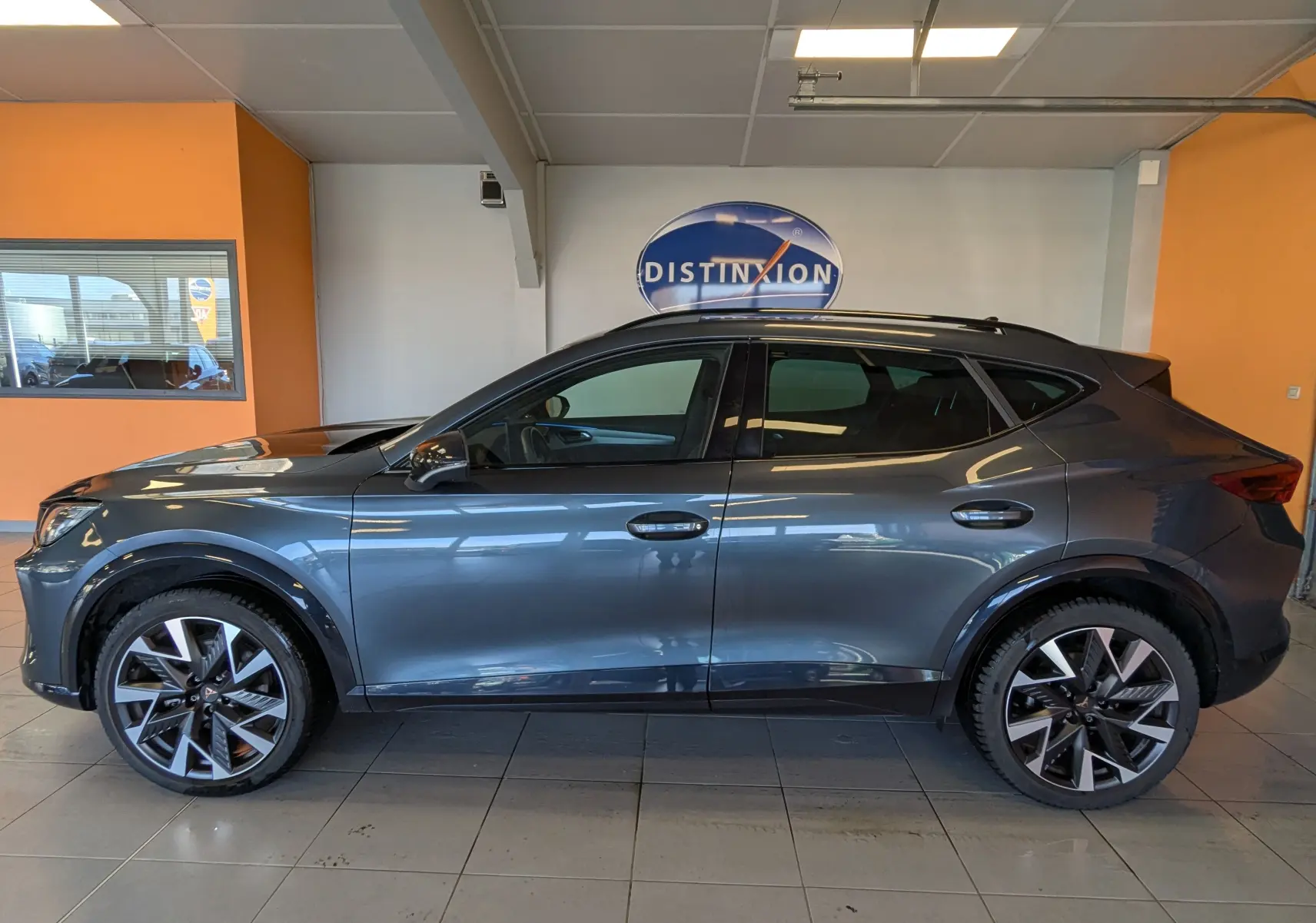 Vue latérale droite d'un CUPRA Formentor gris magnétique métal avec jantes alliage 19 pouces en intérieur showroom.