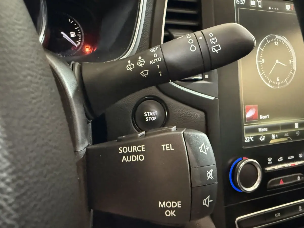 Détail intérieur du volant et commandes audio d’une Renault Mégane Intens gris foncé, avec bouton start/stop visible.