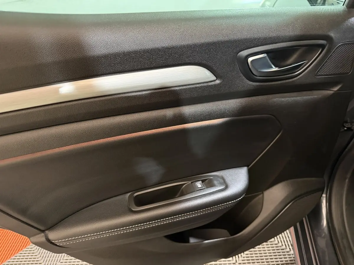 Gros plan sur la porte intérieure côté droit de la Renault Mégane Intens gris foncé, avec poignée et commande de lève-vitre.