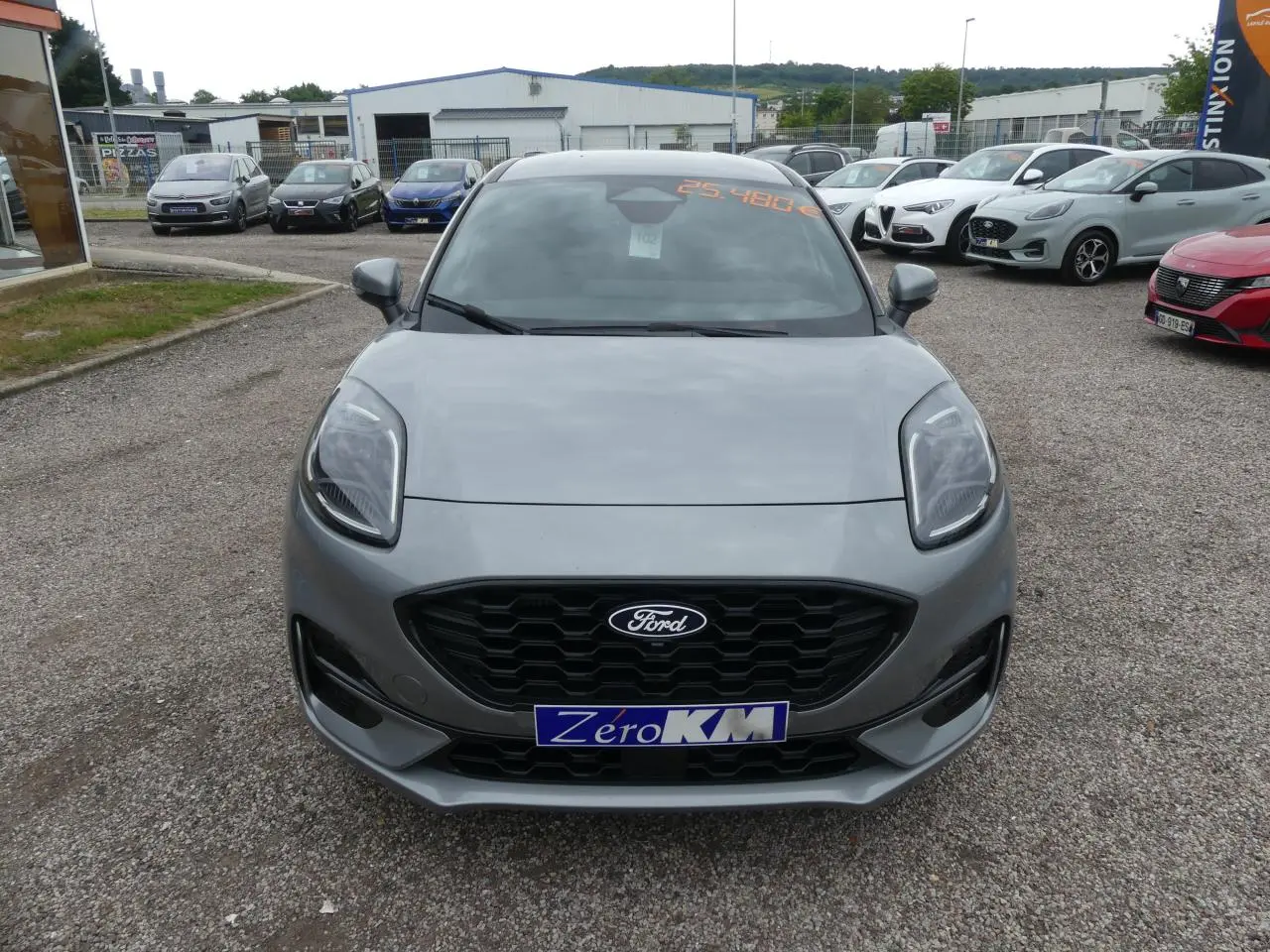 Vue avant d'un Ford Puma gris métallisé avec calandre noire et plaque "Zéro KM" sur un parking extérieur.
