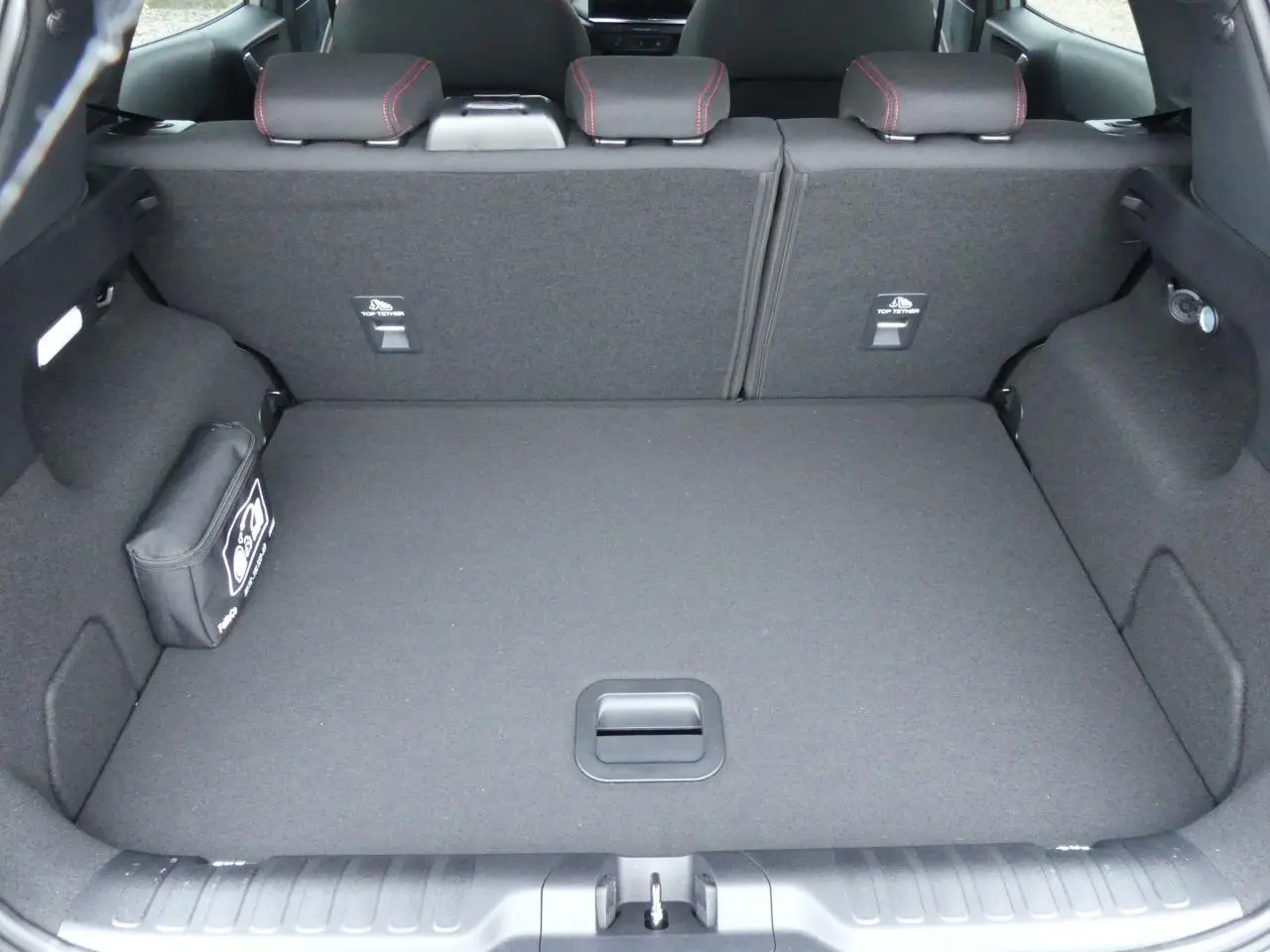 Vue du coffre spacieux et tapis noir du Ford Puma 2025 gris métallisé, avec sièges arrière rabattus et trousse de secours.