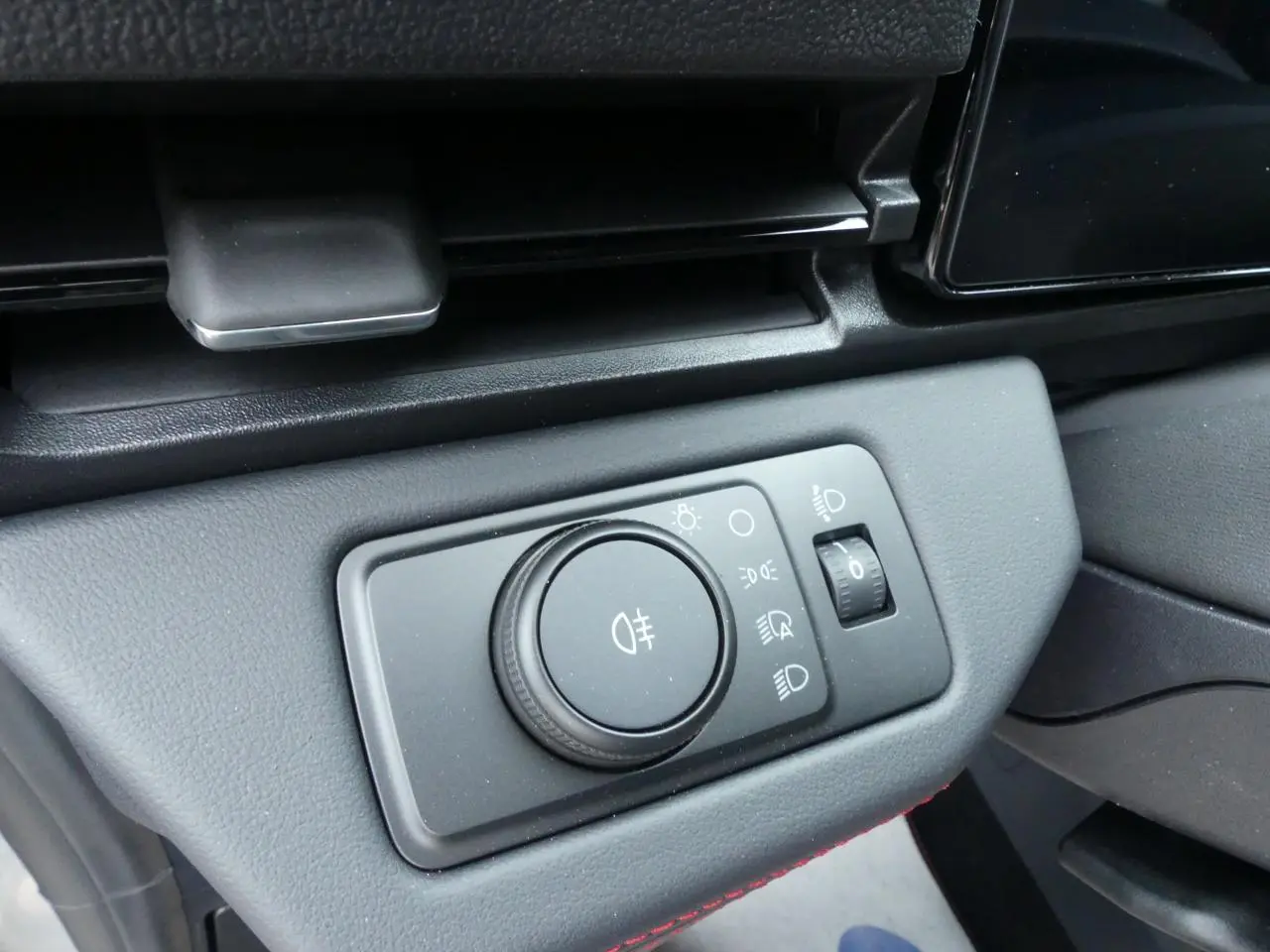Gros plan sur le bouton de réglage des phares dans l'habitacle du Ford Puma 2025 gris métallisé.