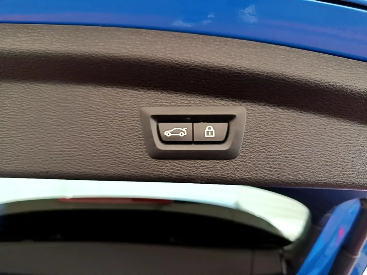 Gros plan sur le bouton d'ouverture et de verrouillage du coffre, intérieur du hayon bleu du BMW X2 sDrive20i M Sport.