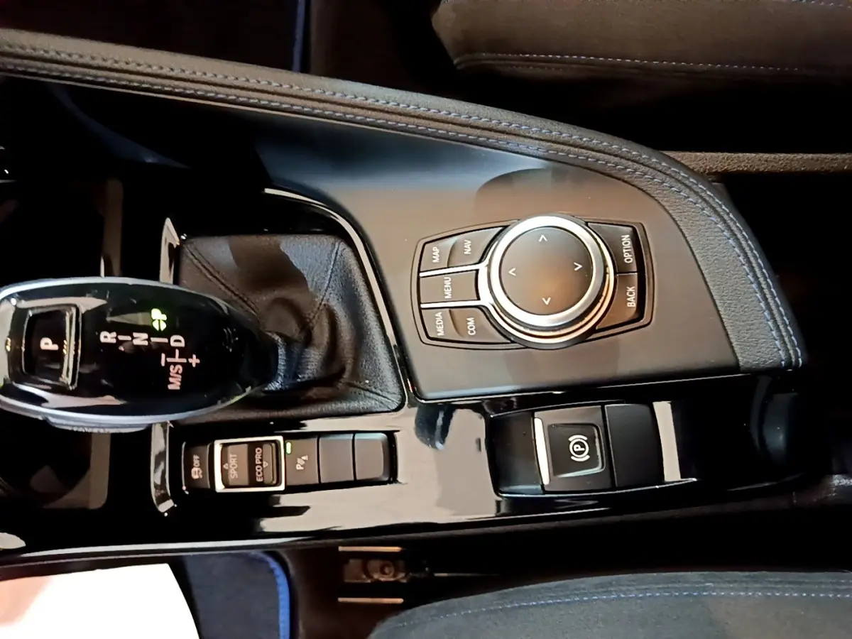 Gros plan sur la console centrale noire brillante du BMW X2 bleu, avec levier de vitesses automatique et molette de contrôle.
