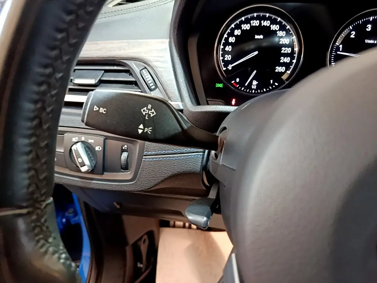 Détail intérieur côté gauche du tableau de bord BMW X2 bleu, avec commandes des phares et compteurs visibles.