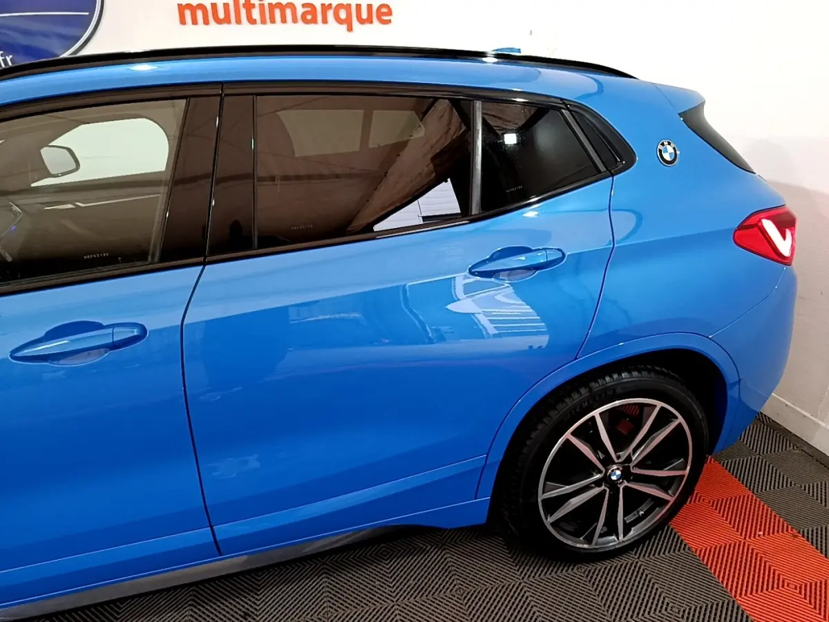Vue latérale droite d'un BMW X2 sDrive20i M Sport bleu avec jantes alliage et logo BMW sur l'aile arrière.