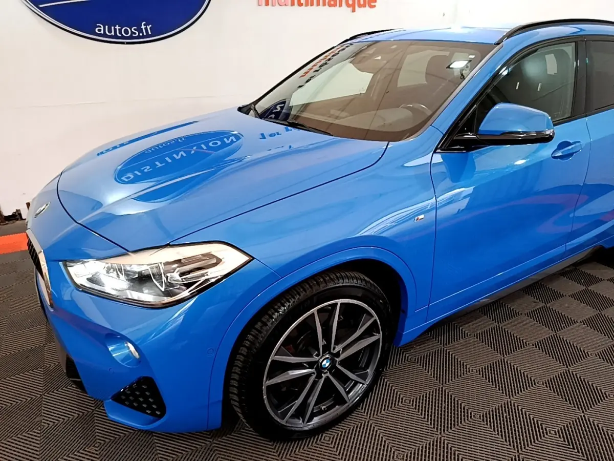 BMW X2 sDrive20i M Sport bleu en 3/4 avant droit, avec jantes alliage et phares LED visibles.