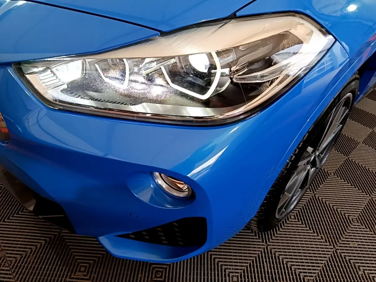 Gros plan sur le phare avant droit bleu vif d'une BMW X2 sDrive20i M Sport avec jante alliage visible.