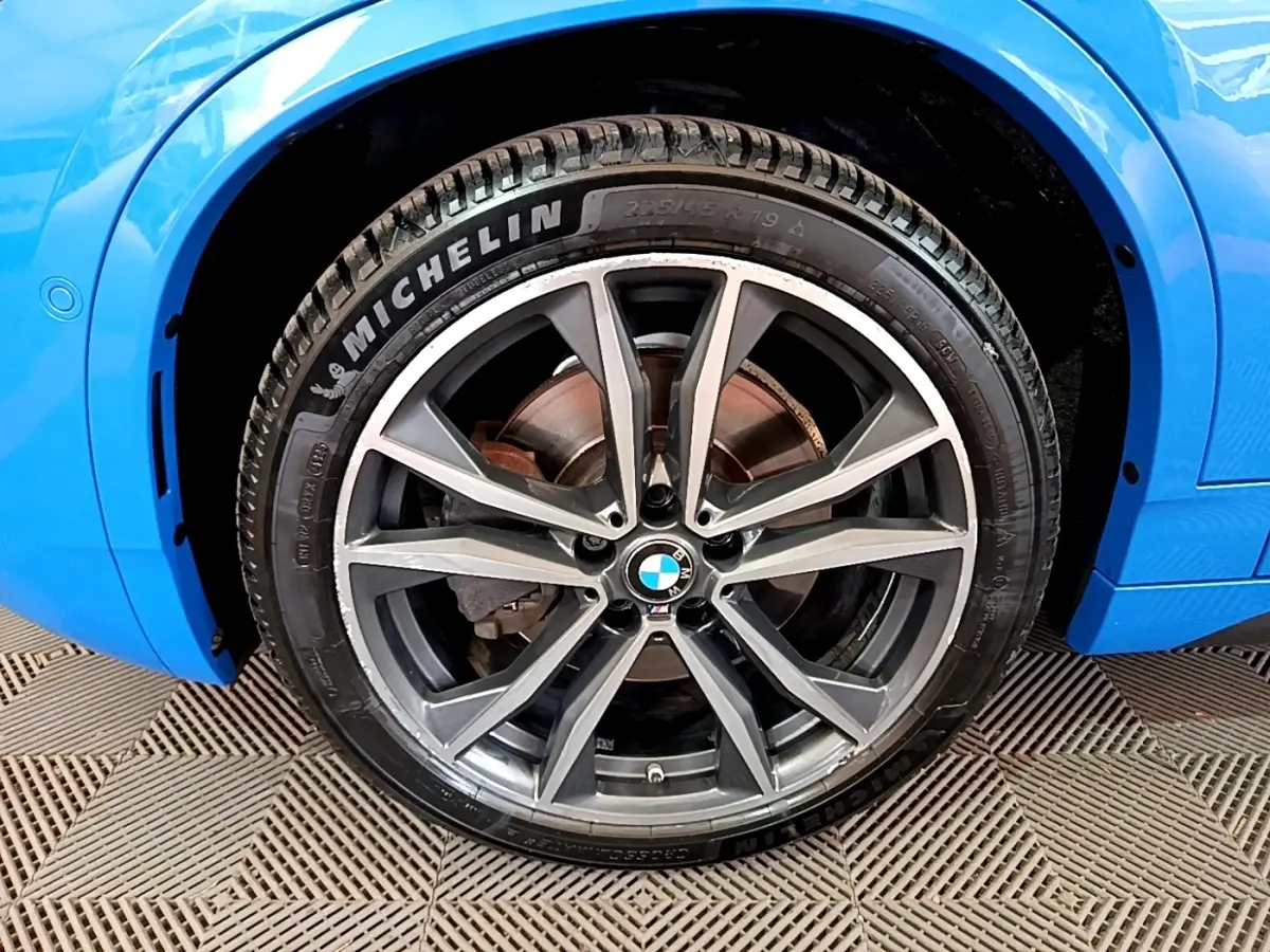 Gros plan sur la roue avant droite d'une BMW X2 bleu avec jante alliage et pneu Michelin visible.