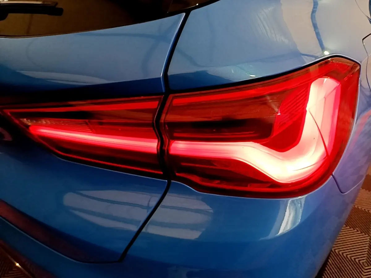 Feu arrière droit allumé sur BMW X2 bleu, vue rapprochée du coin arrière du véhicule.