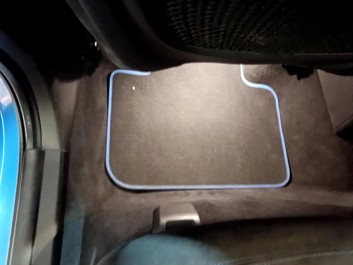 Vue intérieure du plancher côté passager arrière d'une BMW X2 bleu, avec tapis noir bordé de bleu.