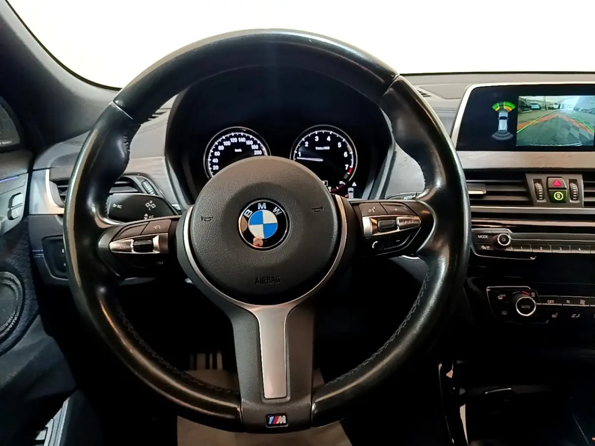 Vue intérieure centrée sur le volant cuir noir BMW M Sport avec tableau de bord et écran de caméra de recul.