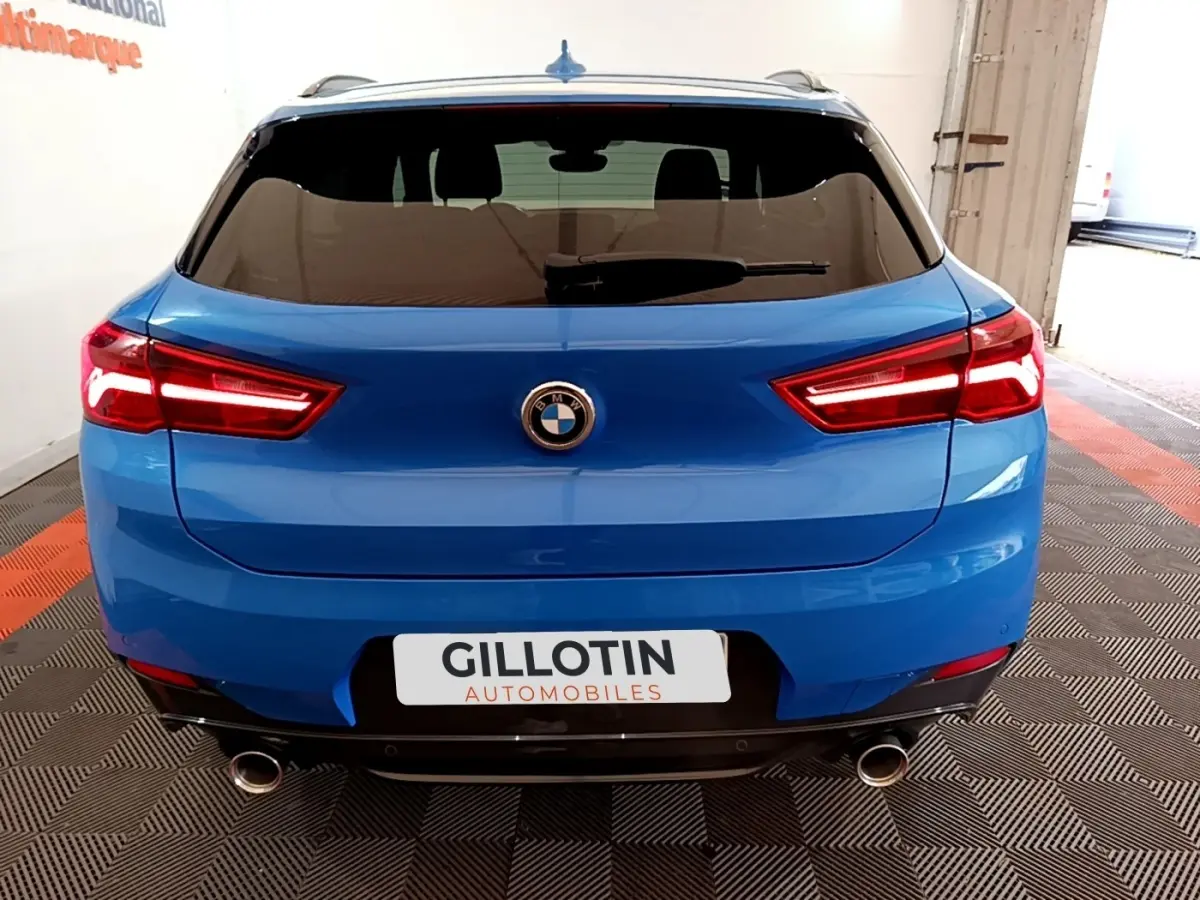 Vue arrière d’un BMW X2 sDrive20i M Sport bleu avec feux LED allumés et double sortie d’échappement chromée.