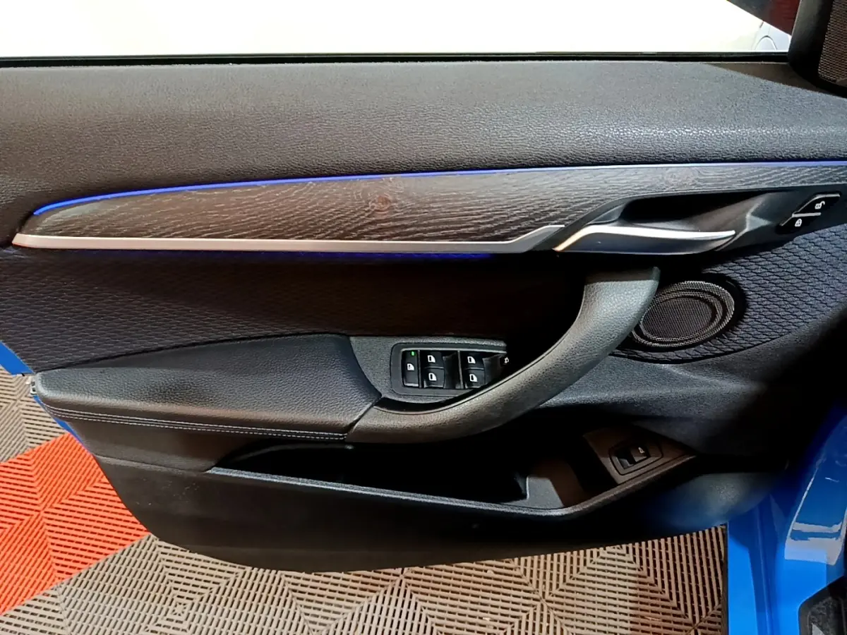 Vue intérieure de la porte avant gauche bleu de la BMW X2 sDrive20i M Sport avec éclairage d'ambiance bleu et commandes vitres.