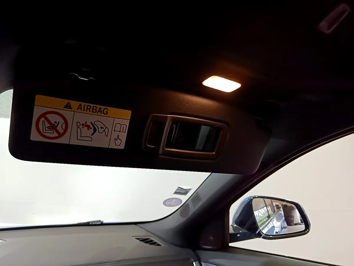 Détail intérieur du pare-soleil côté conducteur avec miroir éclairé et rétroviseur extérieur bleu visible.