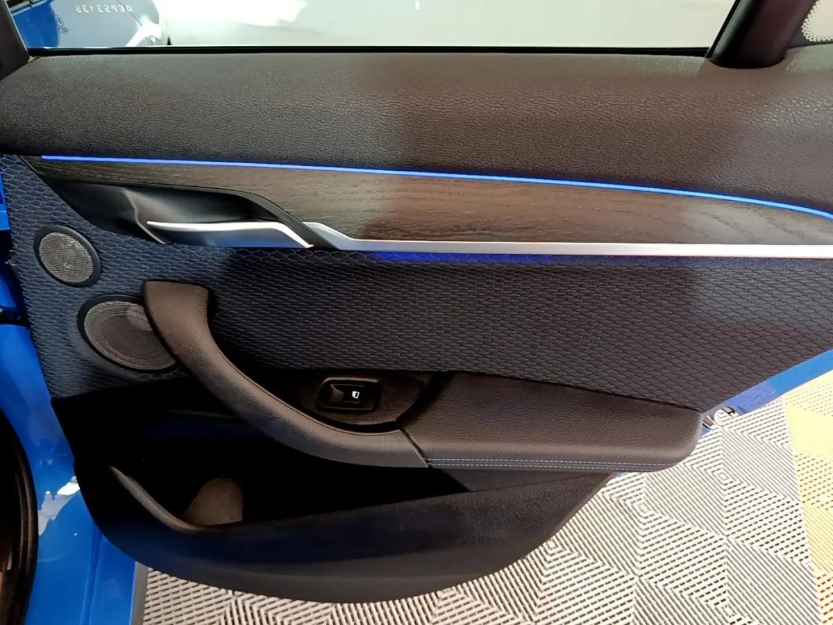 Vue rapprochée de la porte avant gauche d’un BMW X2 bleu, avec éclairage d’ambiance bleu et garniture noire texturée.