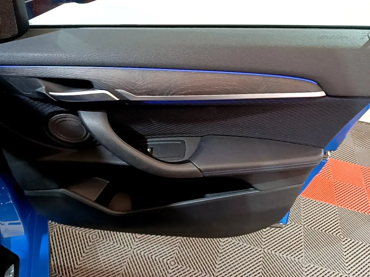 Vue intérieure côté gauche de la porte avant bleu de la BMW X2 avec garniture noire et bande décorative argentée.