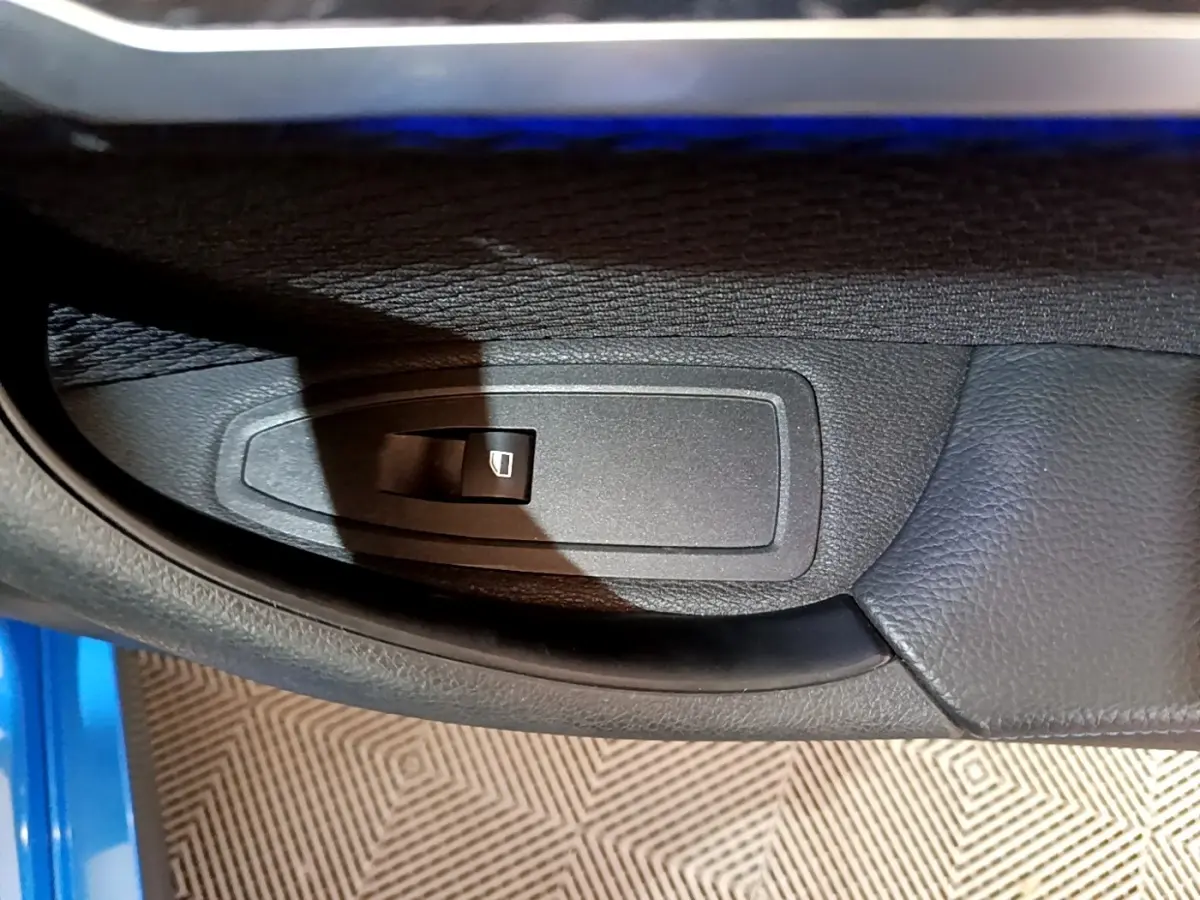 Gros plan sur la commande de lève-vitre côté conducteur d’une BMW X2 sDrive20i M Sport bleu 2019.