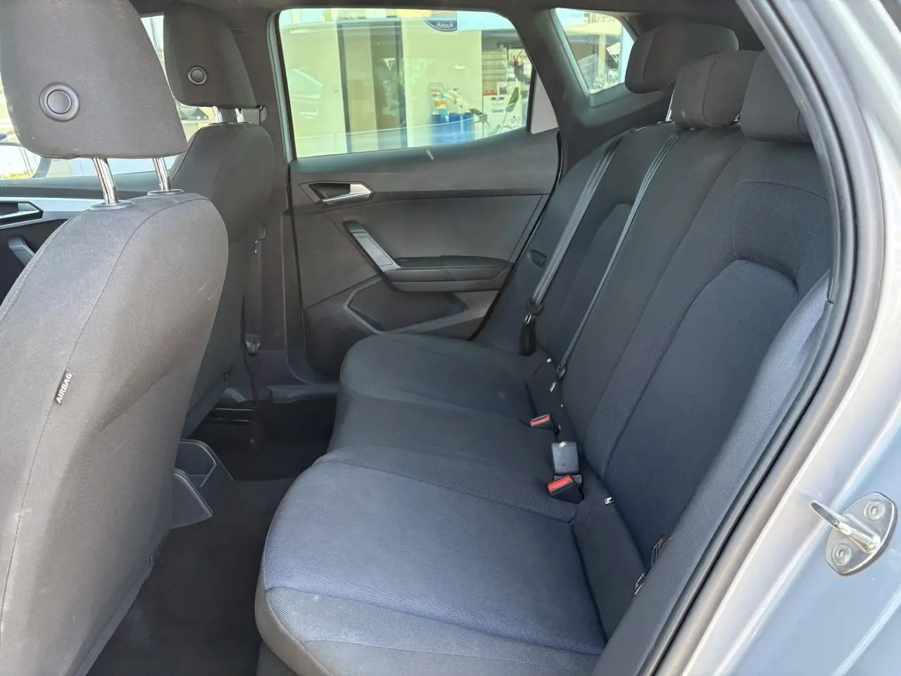 Vue latérale droite de l'intérieur arrière du SEAT Arona 2024 avec sellerie textile noire et appuie-têtes visibles.