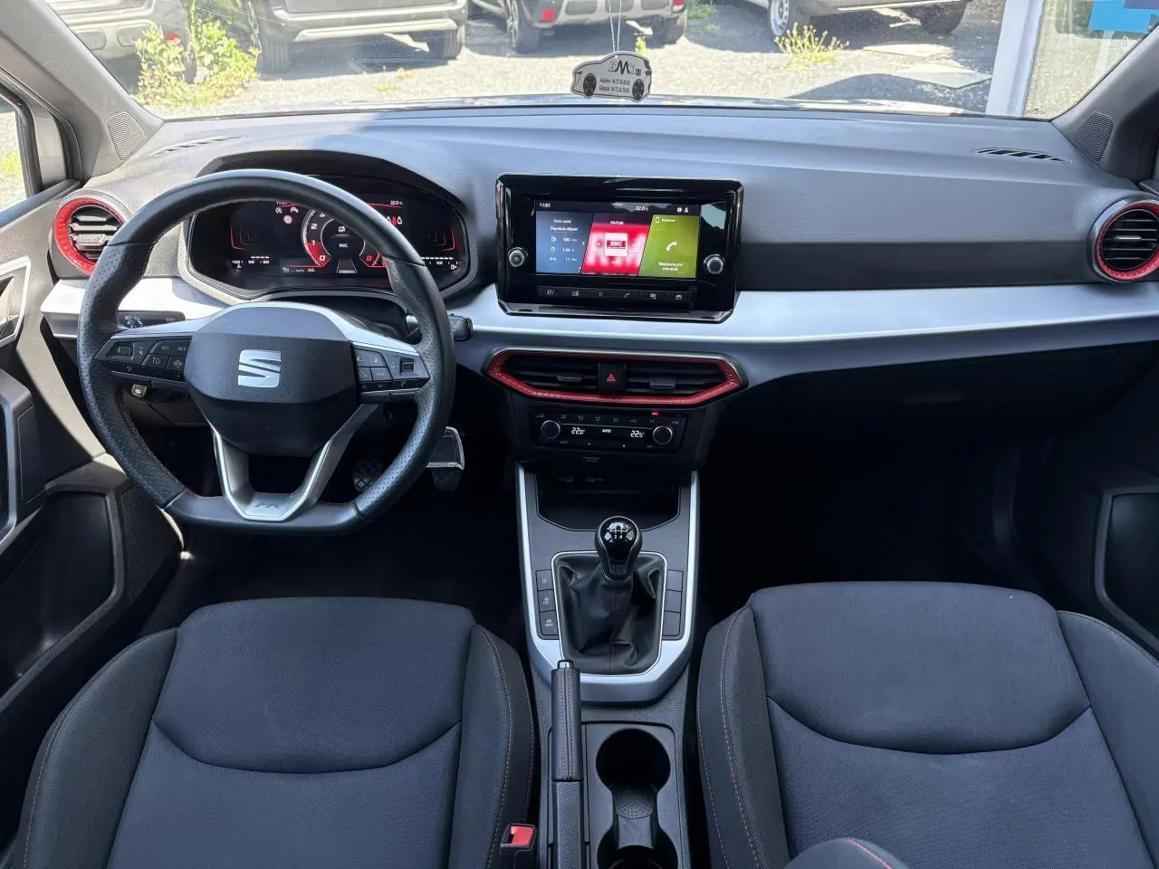 Vue intérieure avant du tableau de bord et volant cuir sport du SEAT ARONA 2024 avec inserts rouges et écran tactile central.